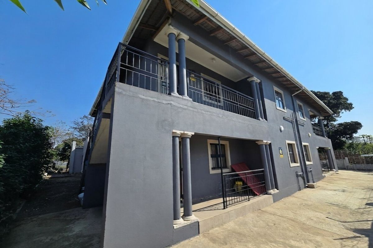 A double-story exterior view of the property featuring a covered ground-floor patio and an upper-level balcony with metal railings and concrete columns.