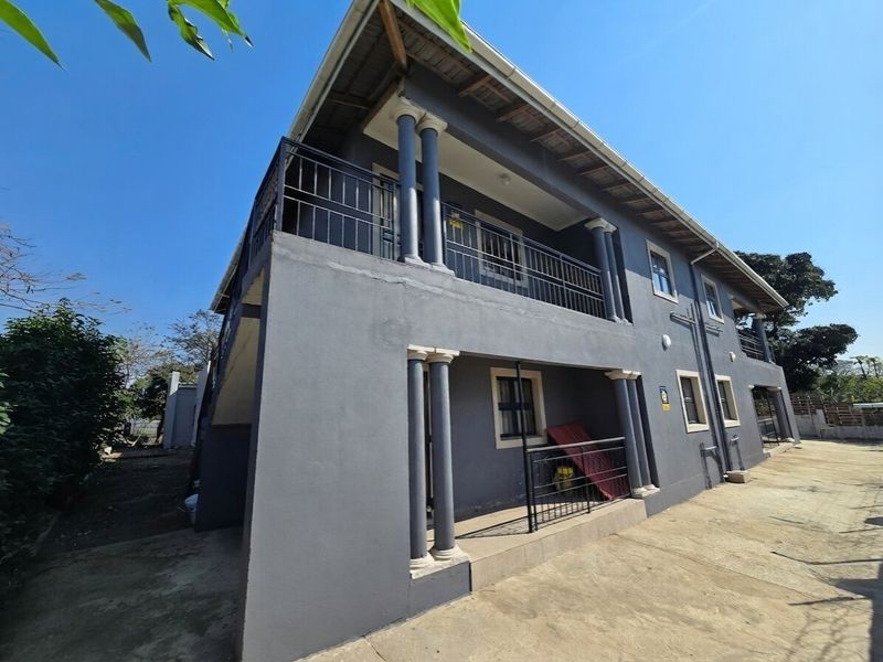 A double-story exterior view of the property featuring a covered ground-floor patio and an upper-level balcony with metal railings and concrete columns.