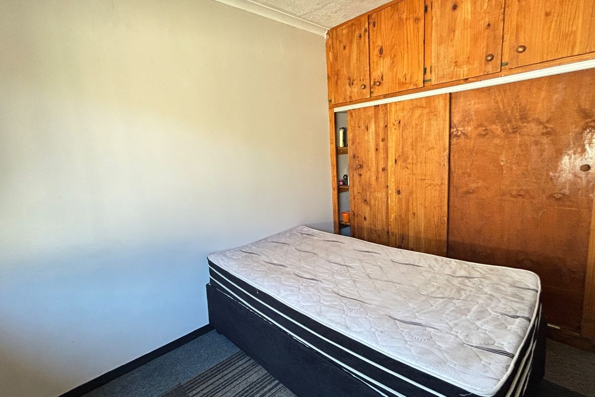 A bedroom featuring built-in wooden cupboards with sliding doors and carpeted flooring, offering a functional space with potential for modernization.