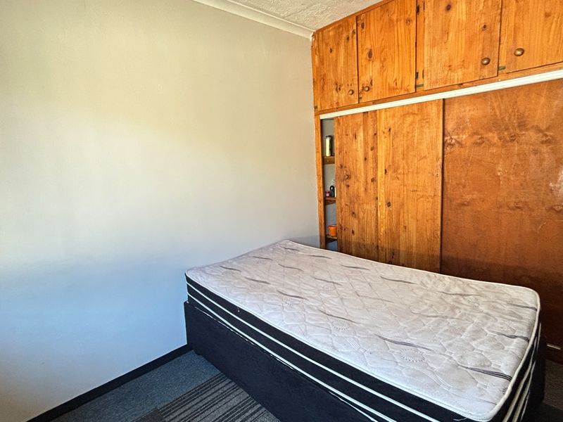 A bedroom featuring built-in wooden cupboards with sliding doors and carpeted flooring, offering a functional space with potential for modernization.