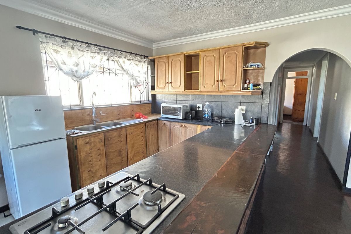 A functional kitchen featuring wooden cabinetry, a gas hob, a breakfast bar, and a tiled backsplash, leading into a hallway via an arched doorway.