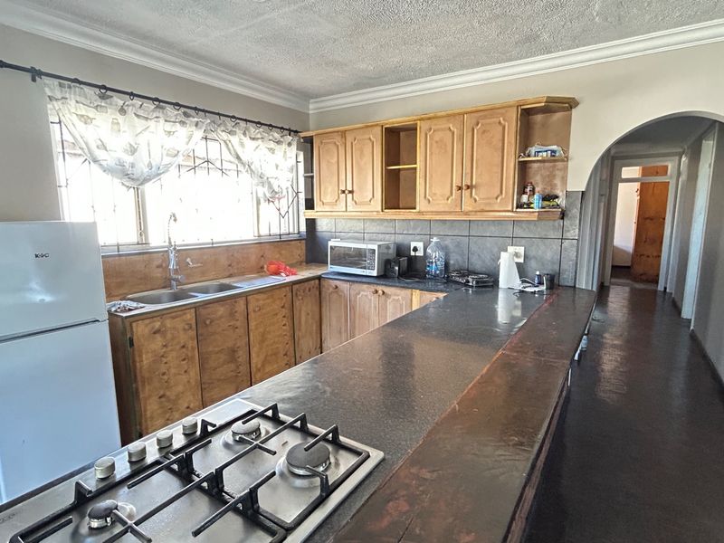 A functional kitchen featuring wooden cabinetry, a gas hob, a breakfast bar, and a tiled backsplash, leading into a hallway via an arched doorway.