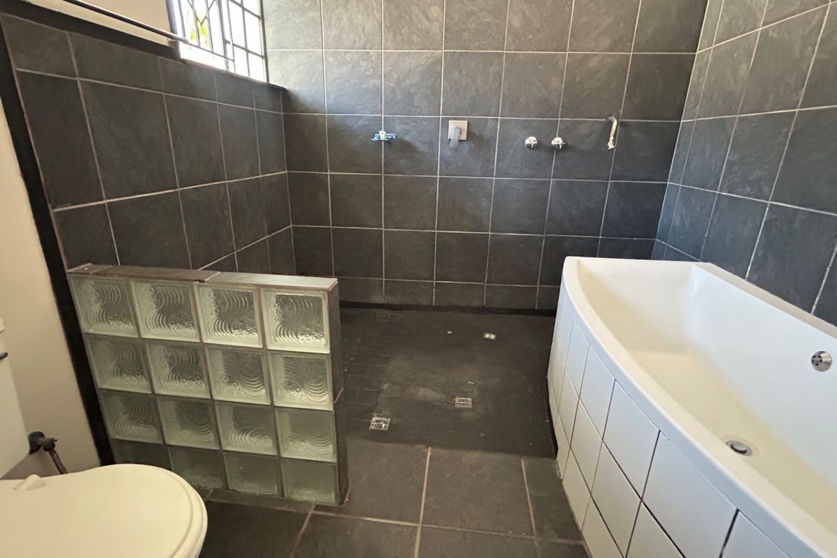 Bathroom featuring a walk-in shower with glass block partition, a built-in bathtub, and dark tiled finishes. Requires minor plumbing fixture replacements.