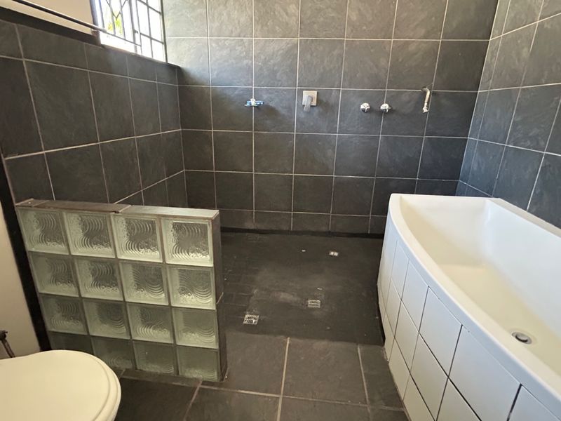 Bathroom featuring a walk-in shower with glass block partition, a built-in bathtub, and dark tiled finishes. Requires minor plumbing fixture replacements.