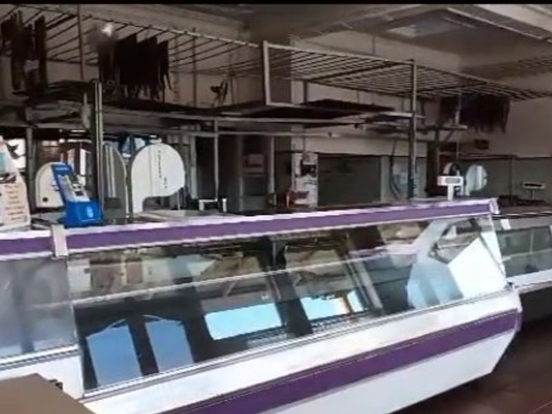 Commercial retail space featuring refrigerated display counters and overhead hanging rails, suitable for a butcher shop or food preparation business.