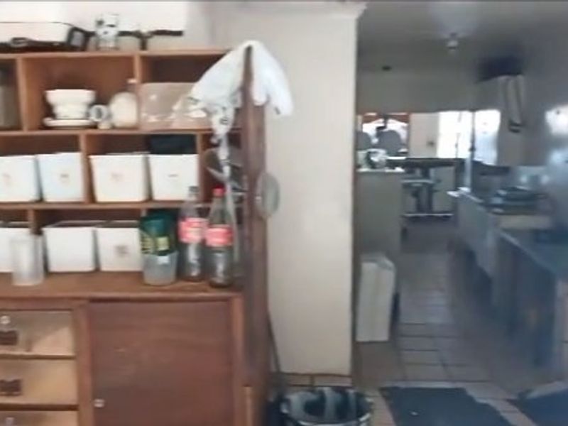 A functional scullery or prep area featuring built-in wooden shelving, tiled floors, and a stainless steel sink, showing signs of age and wear.