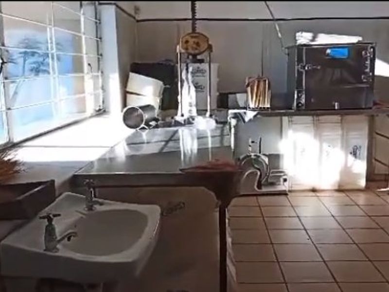 A functional commercial kitchen space featuring stainless steel prep surfaces, a wall-mounted sink, and tiled flooring, suitable for food preparation or utility use.