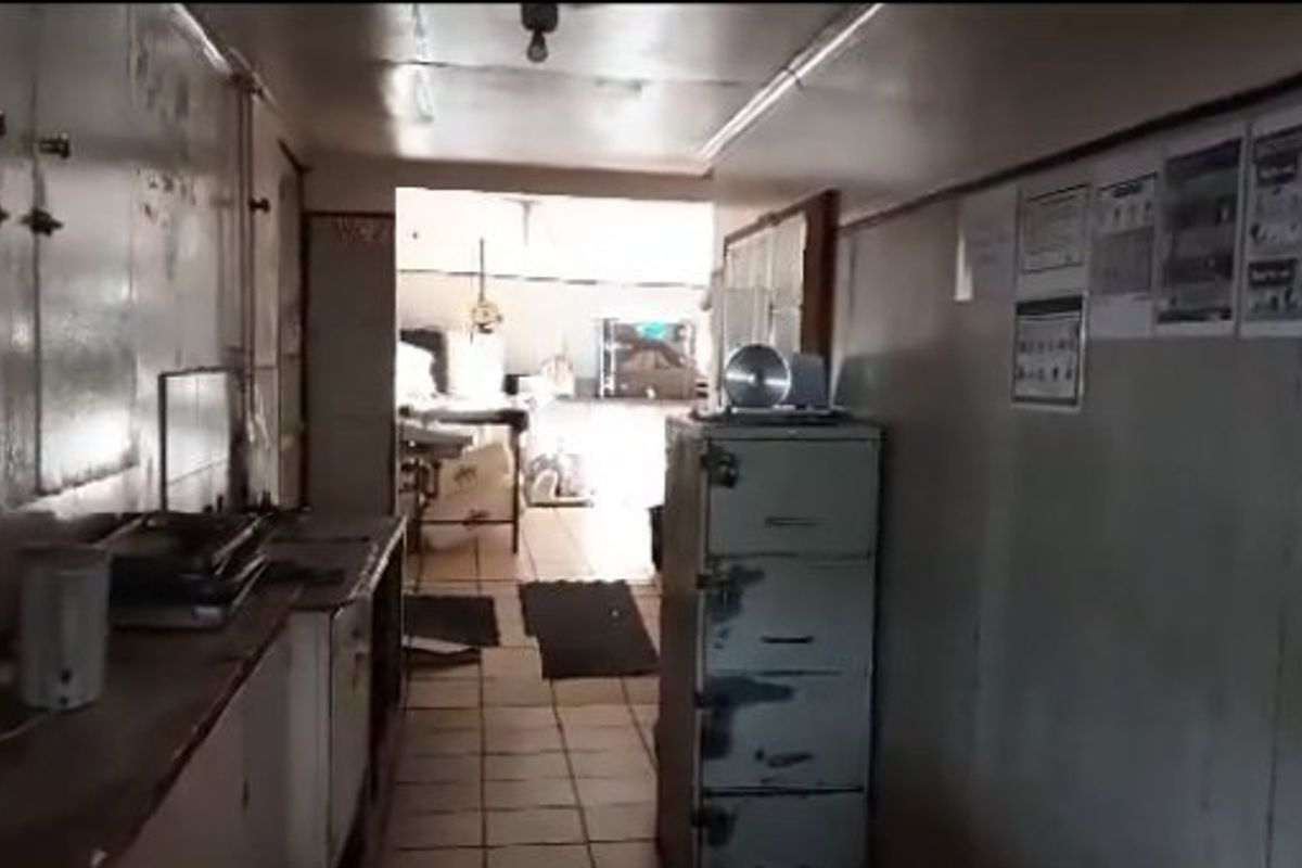 A functional commercial kitchen space featuring tiled flooring and built-in cabinetry, currently showing significant signs of wear and requiring refurbishment.