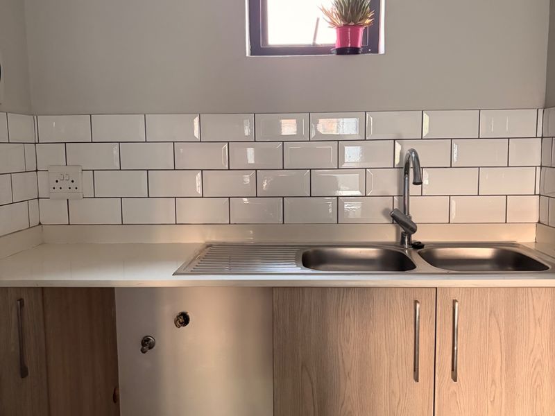 A clean, modern kitchen area featuring light wood cabinetry, a double bowl stainless steel sink, and a classic white subway tile backsplash.