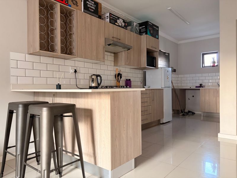 Modern kitchen featuring light wood cabinetry, subway tile backsplash, integrated appliances, and a functional breakfast bar with tiled flooring throughout.