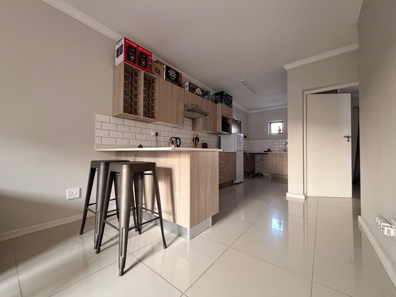 Modern kitchen featuring light wood cabinetry, subway tile backsplash, and a functional breakfast bar with tiled flooring throughout.