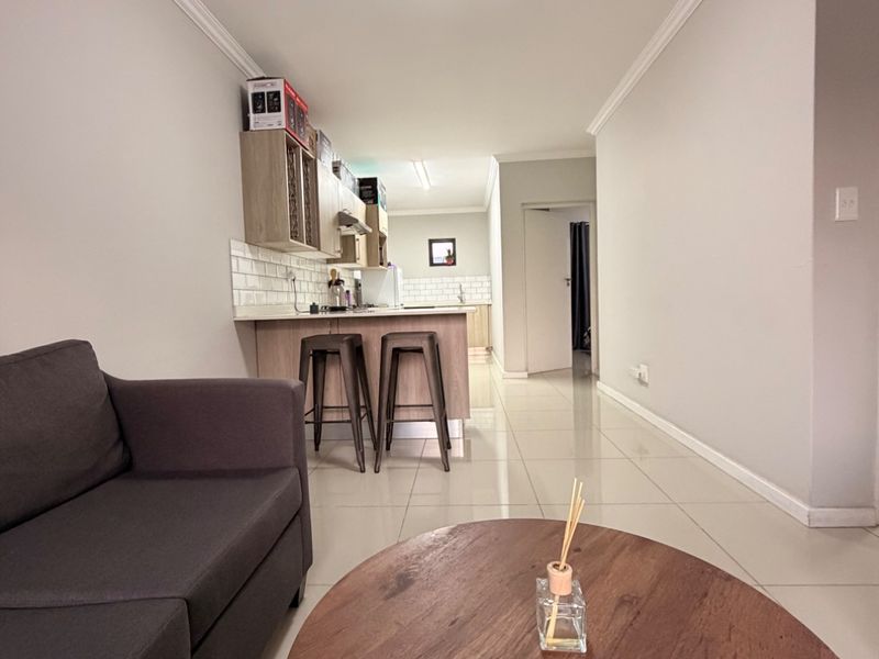 An open-plan living and kitchen area featuring neutral tiled flooring, modern cabinetry, and a breakfast bar island with a subway tile backsplash.