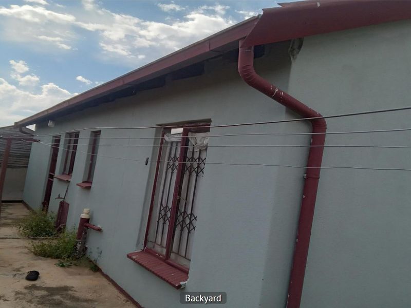 Rear exterior view of the property showing the back wall, guttering system, and security bars on the windows.