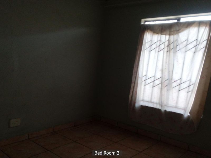 An empty bedroom featuring tiled flooring and a window with security bars, requiring cosmetic updates and improved lighting.