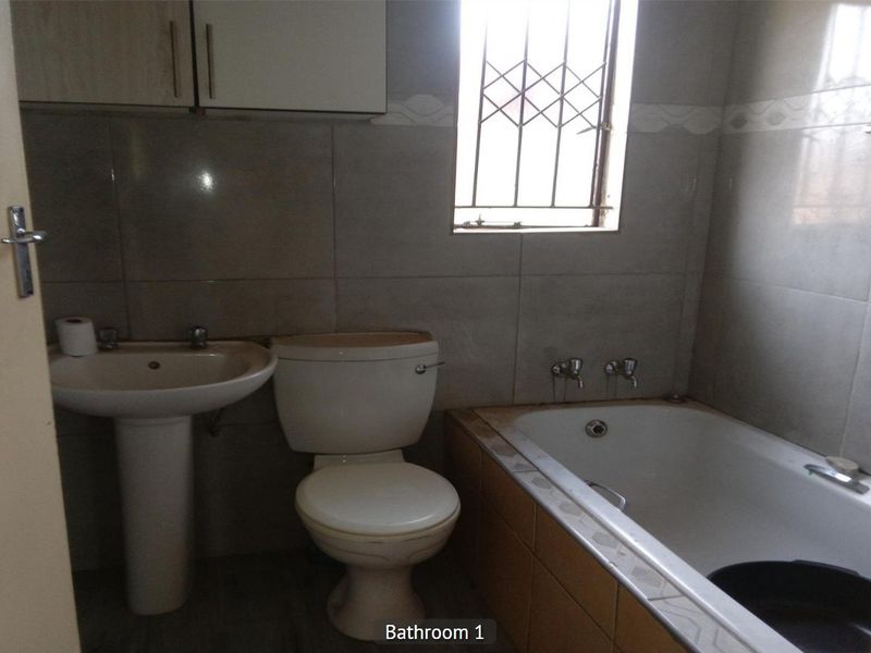A functional bathroom featuring a pedestal basin, toilet, and built-in bathtub with tiled walls and a security-fitted window.