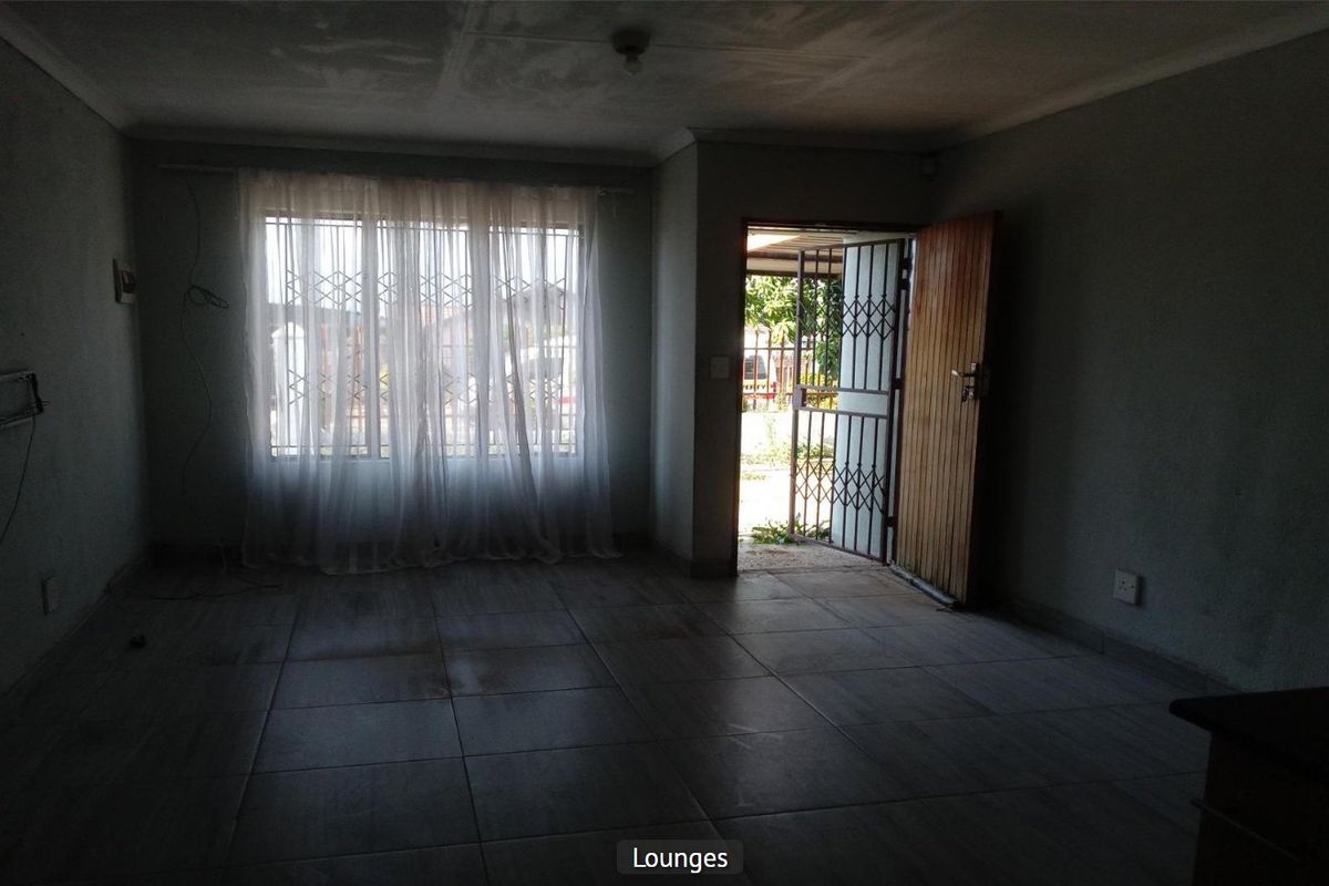 An empty living room featuring tiled flooring, a security gate at the entrance, and a timber door, requiring cosmetic updates and improved lighting.