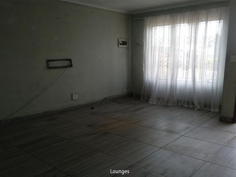 An empty living room featuring tiled flooring, security gate on the window, and basic electrical fixtures, ready for a fresh update.