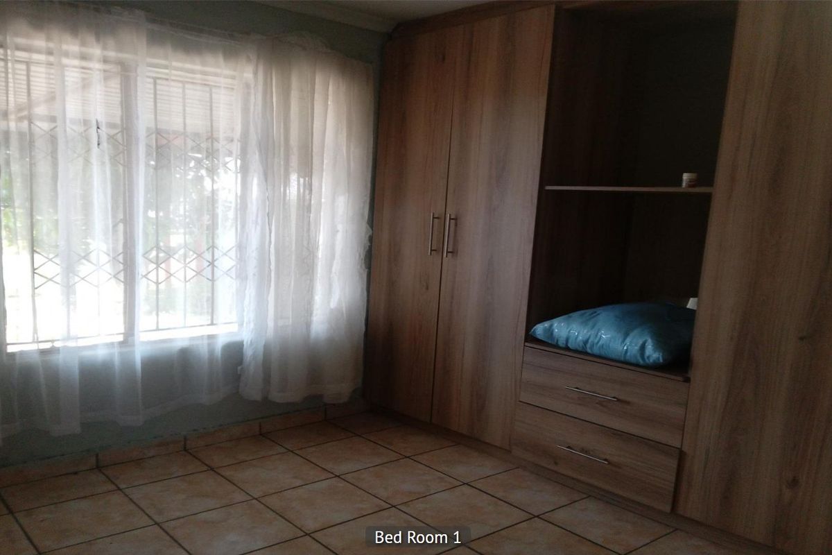 Bedroom featuring built-in wooden cupboards, tiled flooring, and a window fitted with security bars.
