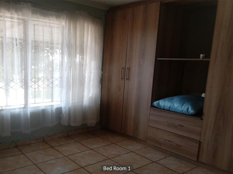 Bedroom featuring built-in wooden cupboards, tiled flooring, and a window fitted with security bars.