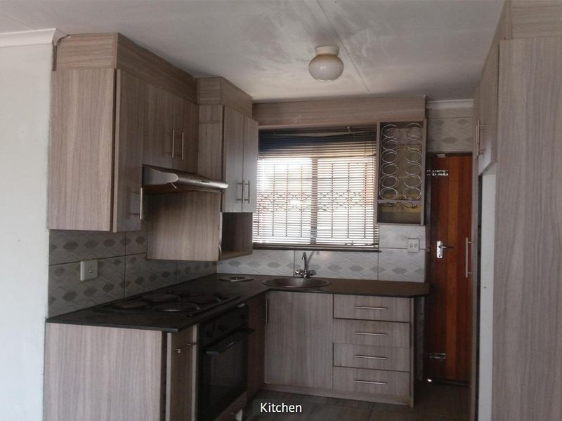 A functional kitchen featuring wood-look cabinetry, built-in oven and hob, tiled backsplash, and a stainless steel sink with natural light from the window.