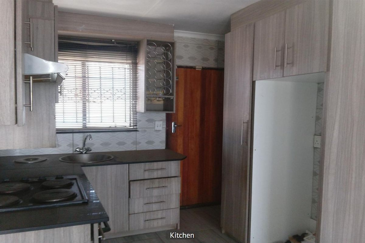 A functional kitchen featuring light wood-grain cabinetry, dark laminate countertops, a built-in electric hob, and an integrated extractor fan.