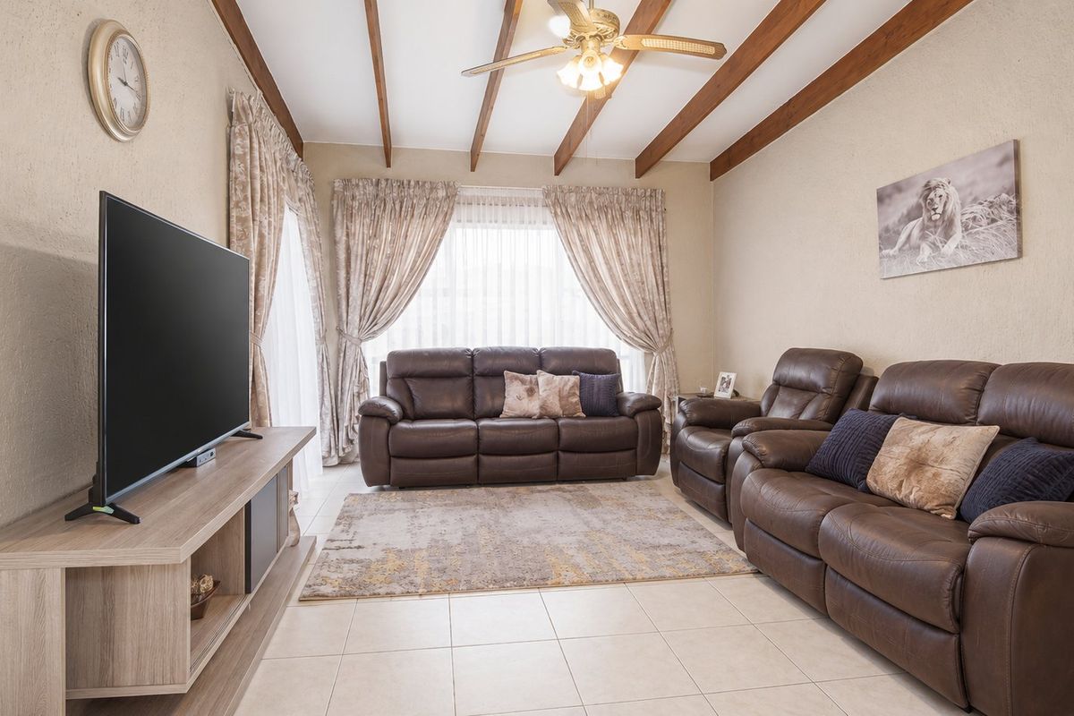 A comfortable living room featuring exposed timber ceiling beams, a ceiling fan, tiled flooring, and a sliding glass door providing natural light.
