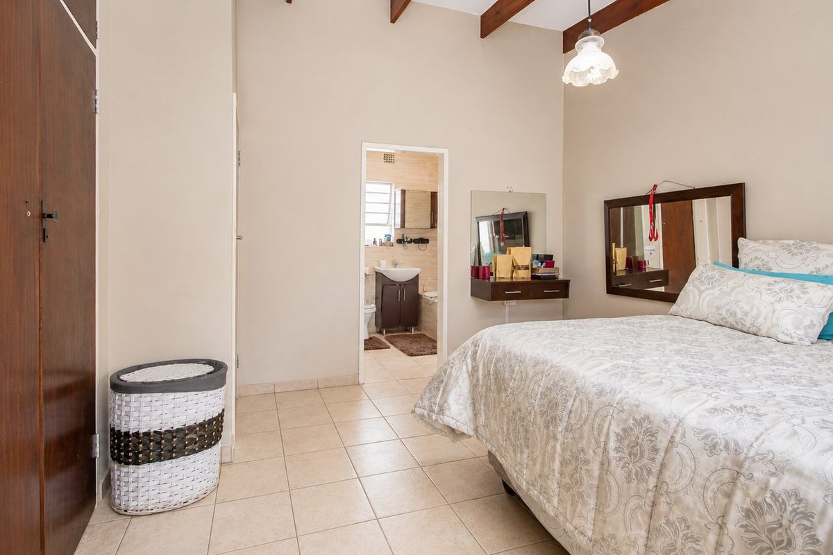 Spacious bedroom featuring tiled flooring, exposed timber ceiling beams, and a built-in wardrobe, with direct access to an en-suite bathroom.
