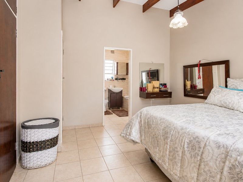 Spacious bedroom featuring tiled flooring, exposed timber ceiling beams, and a built-in wardrobe, with direct access to an en-suite bathroom.