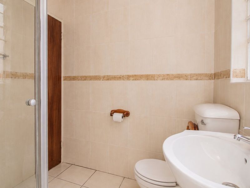 A functional bathroom featuring a shower enclosure, pedestal basin, and toilet with neutral wall and floor tiling.