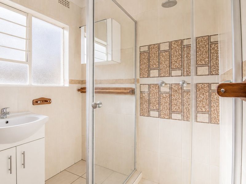 A functional bathroom featuring a vanity basin, a glass-enclosed shower with decorative tiled accents, and neutral wall and floor tiling.