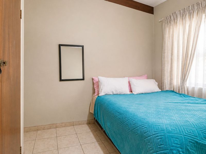 A functional bedroom featuring tiled flooring, a wooden door, and a window with curtain rails, providing a neutral base for personalization.