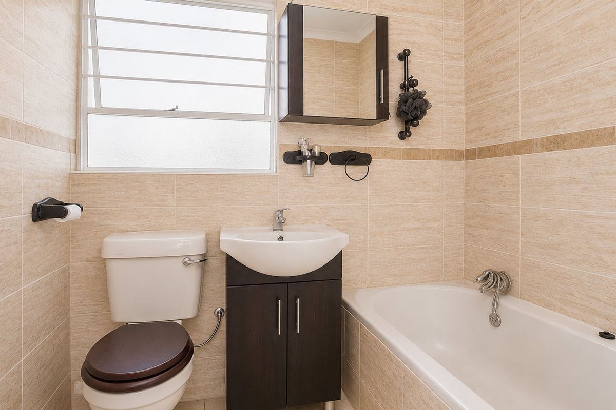 A well-maintained bathroom featuring neutral wall tiling, a built-in vanity with storage, a bathtub, and a louvered window for natural ventilation.