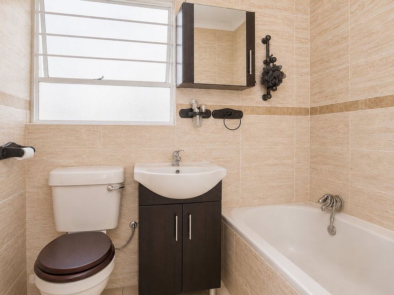 A well-maintained bathroom featuring neutral wall tiling, a built-in vanity with storage, a bathtub, and a louvered window for natural ventilation.