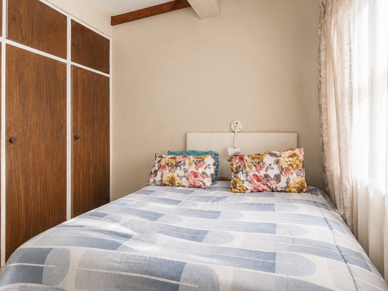A compact bedroom featuring built-in wooden cupboards and an exposed timber ceiling beam, providing a functional and cozy sleeping space.