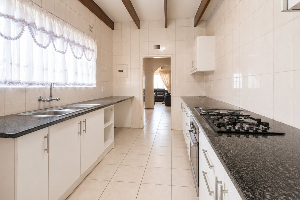 Functional kitchen featuring granite countertops, gas hob, built-in oven, and double sink, complemented by exposed timber ceiling beams and full-height wall tiling.
