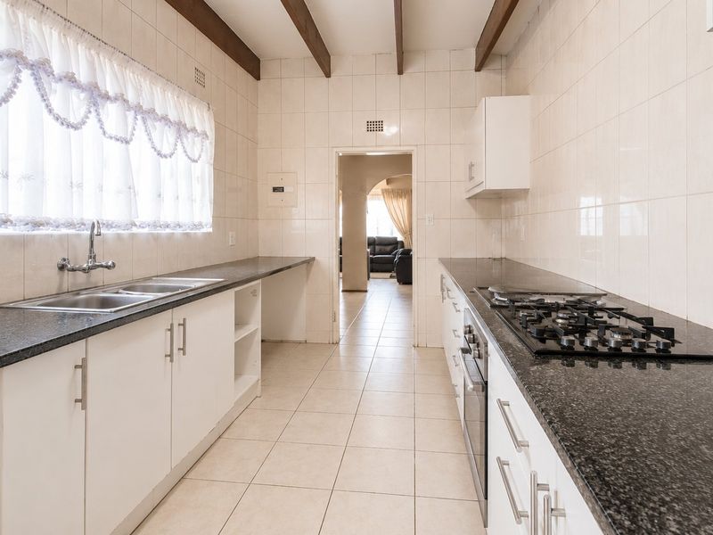 Functional kitchen featuring granite countertops, gas hob, built-in oven, and double sink, complemented by exposed timber ceiling beams and full-height wall tiling.