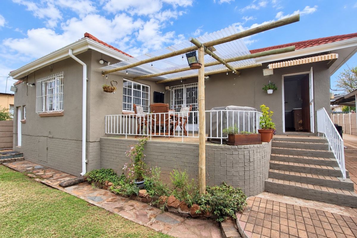 Rear view of the house featuring a raised patio with a timber pergola, metal railings, and paved access stairs leading to the garden.
