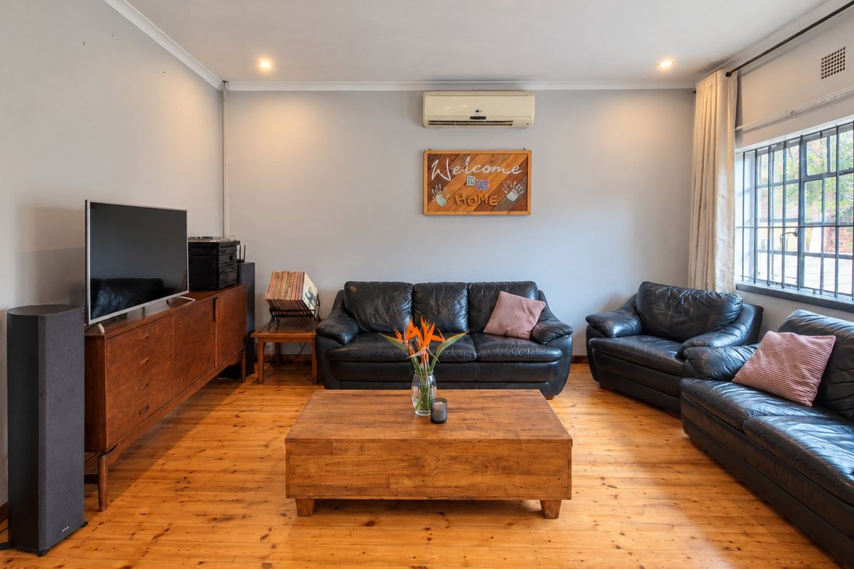 A well-maintained living room featuring polished timber flooring, recessed downlighting, and a wall-mounted split-system air conditioner.
