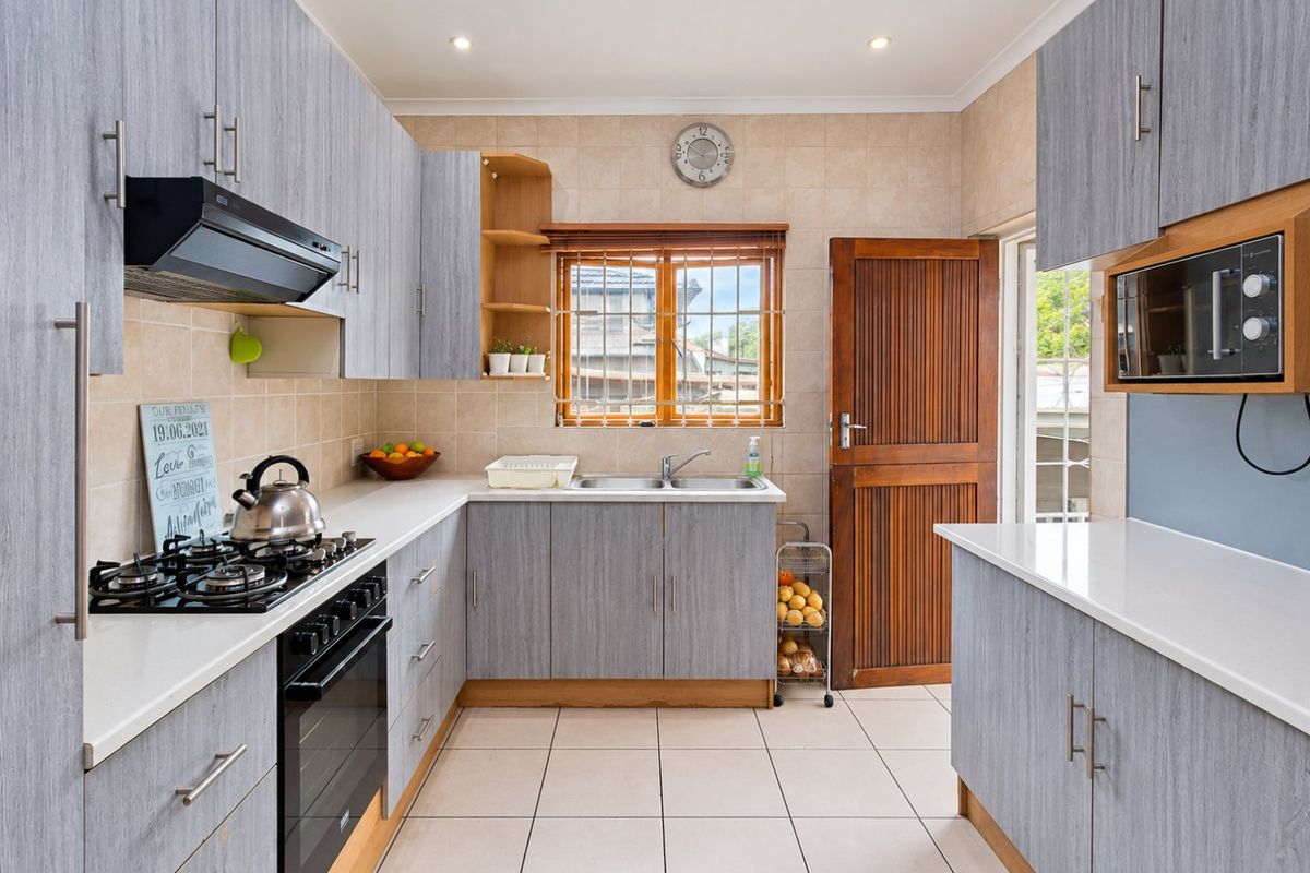 A functional kitchen featuring grey wood-grain cabinetry, white countertops, a gas hob with extractor, and tiled flooring with direct access to the exterior.