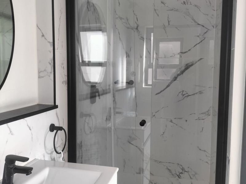 Modern bathroom featuring marble-look wall tiles, a black-framed glass shower enclosure, and a contemporary vanity basin with black fixtures.