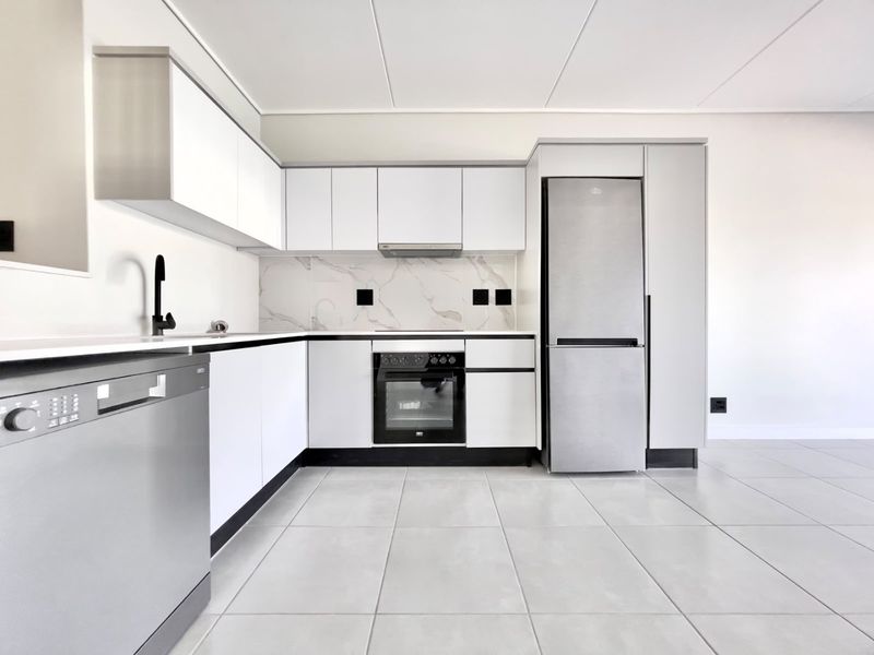 Modern, minimalist kitchen featuring white cabinetry, marble-look splashback, integrated oven, extractor fan, and sleek black fixtures with neutral tiled flooring.