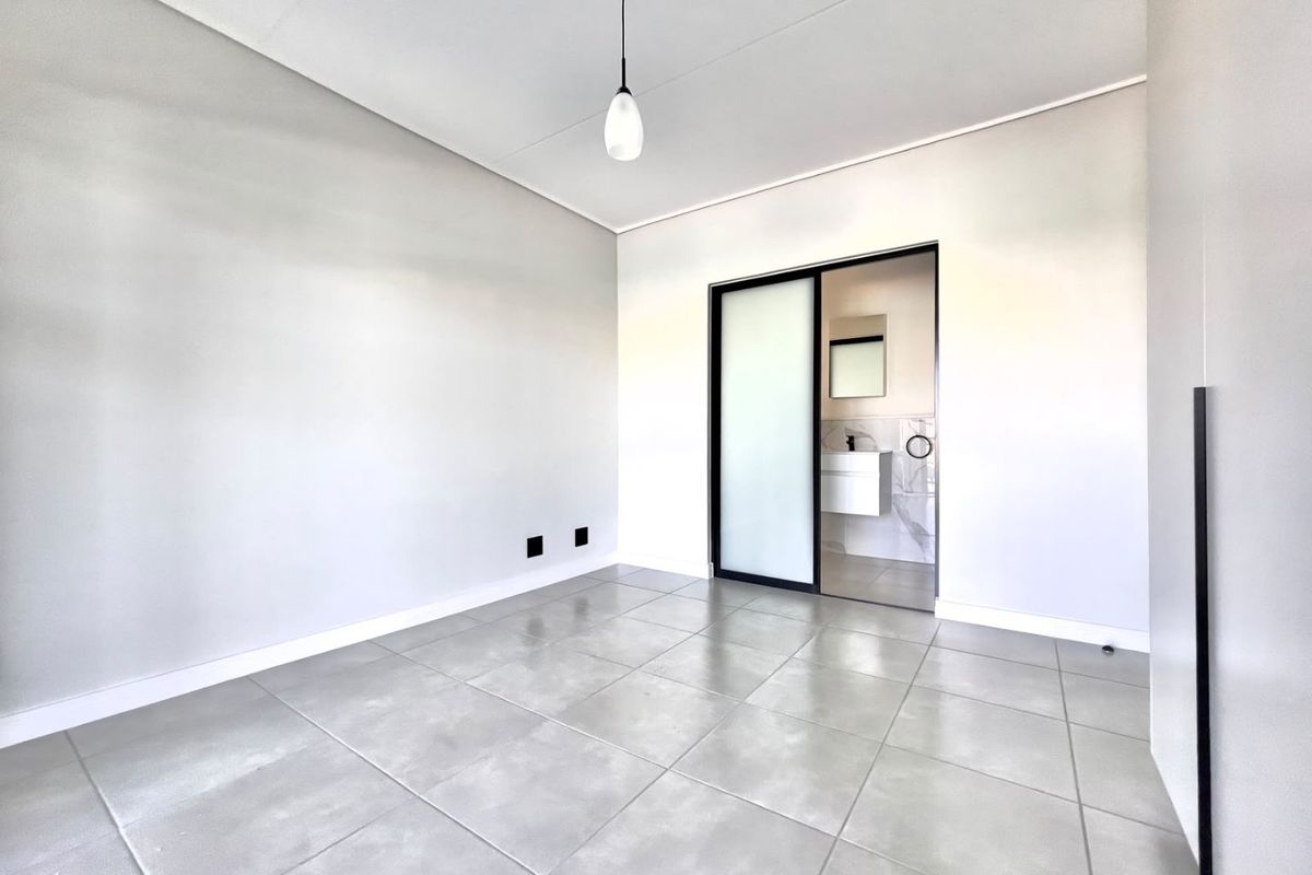 A bright, modern bedroom featuring large format floor tiles, a sleek sliding door leading to an en-suite bathroom, and minimalist built-in cabinetry.