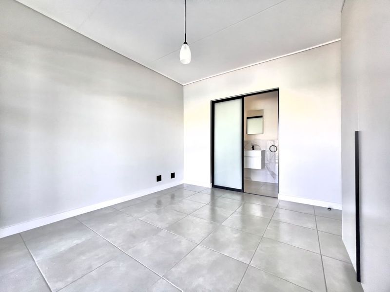 A bright, modern bedroom featuring large format floor tiles, a sleek sliding door leading to an en-suite bathroom, and minimalist built-in cabinetry.