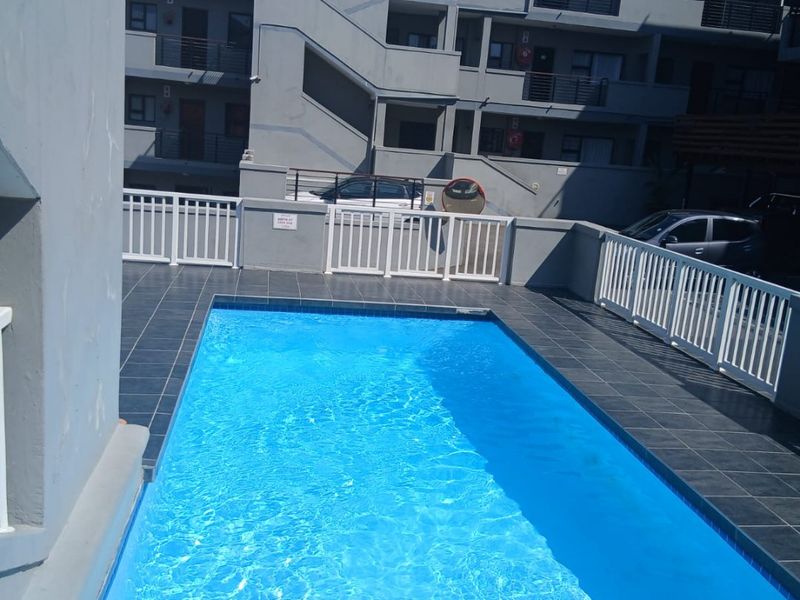 A communal swimming pool area featuring a tiled deck and safety railings, situated within an apartment complex.