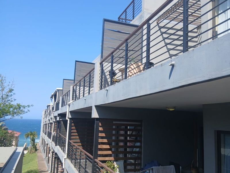 A side view of a multi-story apartment complex featuring tiered balconies with metal railings and timber privacy screens, overlooking a coastal landscape.
