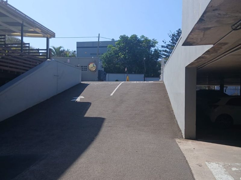 An asphalt driveway leading to a covered parking area with concrete retaining walls and a safety mirror for visibility.