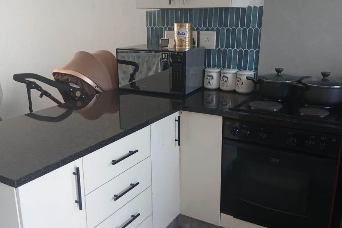 A compact kitchen featuring white cabinetry, black granite countertops, a built-in oven with electric hob, and a decorative blue tiled backsplash.