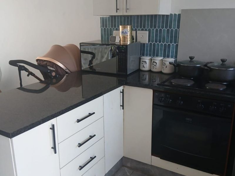 A compact kitchen featuring white cabinetry, black granite countertops, a built-in oven with electric hob, and a decorative blue tiled backsplash.