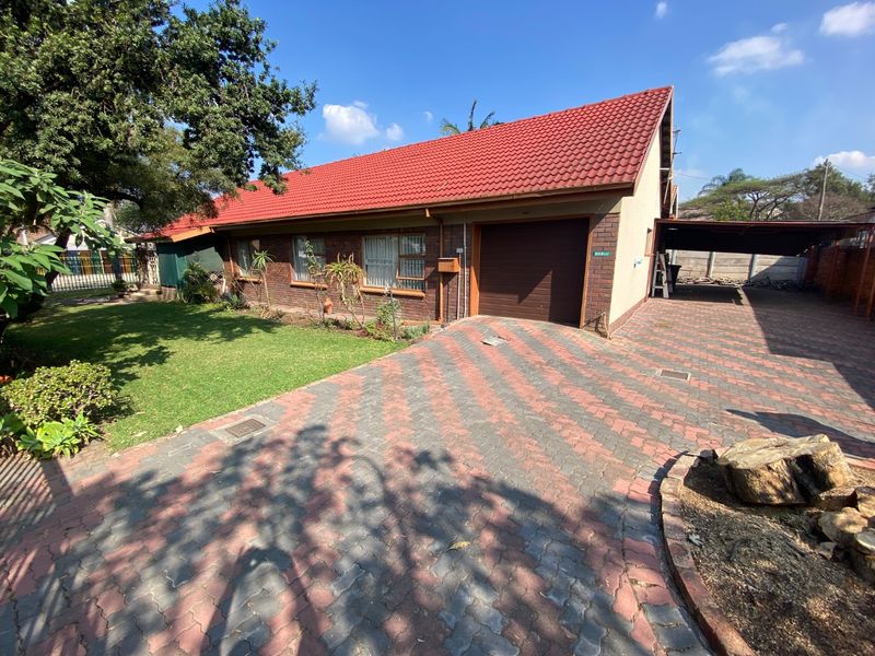 Front view of a brick house featuring a tiled roof, paved driveway, single garage, and an attached carport.