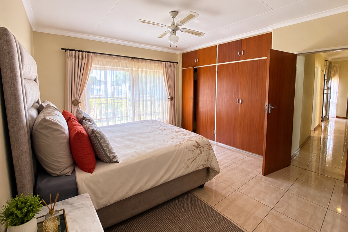 Spacious bedroom featuring tiled flooring, a ceiling fan, and extensive built-in wooden wardrobe storage.